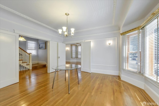 dining space featuring stairway, light wood-style floors, an inviting chandelier, and a raised ceiling