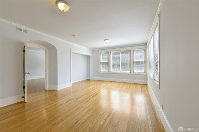spare room with arched walkways, baseboards, visible vents, and light wood-type flooring