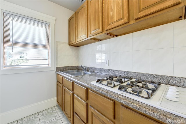 kitchen with tasteful backsplash, a sink, brown cabinets, baseboards, and white gas cooktop
