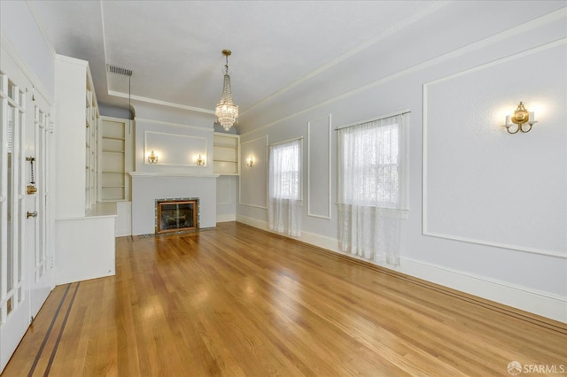 unfurnished living room featuring a notable chandelier, baseboards, a fireplace with flush hearth, visible vents, and wood finished floors