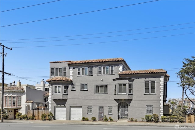 mediterranean / spanish house with a tiled roof, a garage, stucco siding, and fence