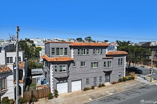 view of property featuring a tiled roof, an attached garage, fence, and stucco siding