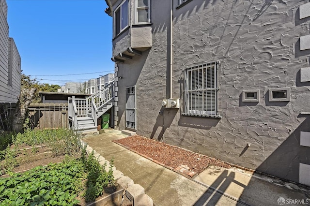 view of side of property featuring fence, stairway, and stucco siding
