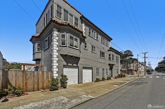 view of front of house with a tiled roof, a garage, stucco siding, and fence