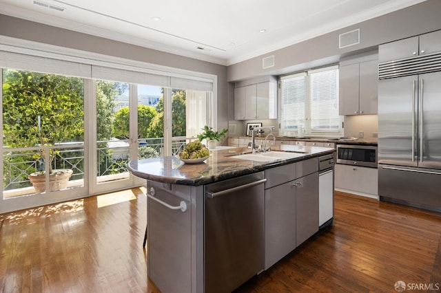 kitchen with dark wood-type flooring, an island with sink, white cabinets, built in appliances, and sink