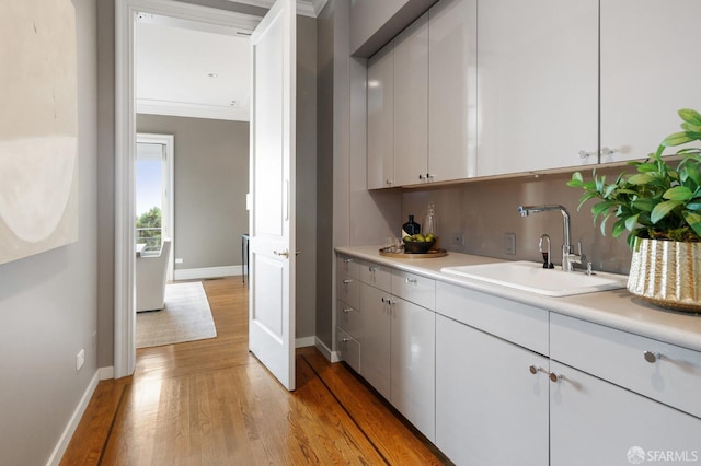 kitchen with decorative backsplash, white cabinetry, light hardwood / wood-style flooring, ornamental molding, and sink