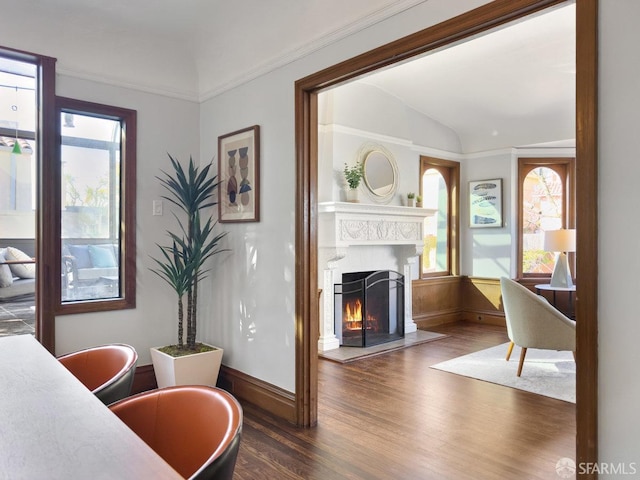 interior space featuring lofted ceiling, a warm lit fireplace, baseboards, and wood finished floors