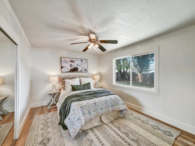 bedroom with ceiling fan, a textured ceiling, wood finished floors, baseboards, and ornamental molding