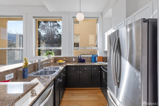 kitchen with sink, appliances with stainless steel finishes, dark stone countertops, white cabinetry, and hanging light fixtures