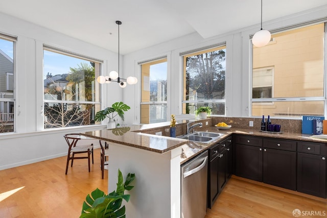 kitchen featuring sink, hanging light fixtures, light hardwood / wood-style floors, stainless steel dishwasher, and dark stone counters