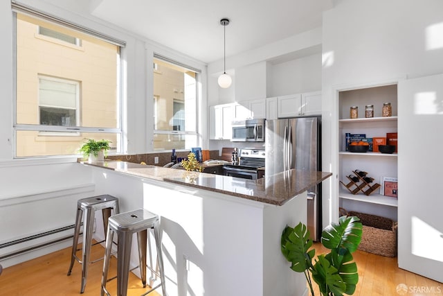 kitchen with white cabinets, dark stone counters, hanging light fixtures, kitchen peninsula, and stainless steel appliances