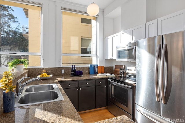 kitchen with sink, white cabinetry, hanging light fixtures, dark stone countertops, and stainless steel appliances