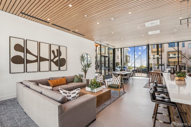 living area with concrete flooring, a wall of windows, wooden ceiling, and baseboards