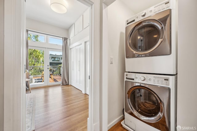 laundry area with stacked washing maching and dryer, baseboards, laundry area, and wood finished floors