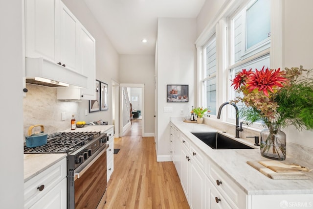 kitchen with tasteful backsplash, light wood-style floors, stainless steel range with gas stovetop, a sink, and white cabinetry