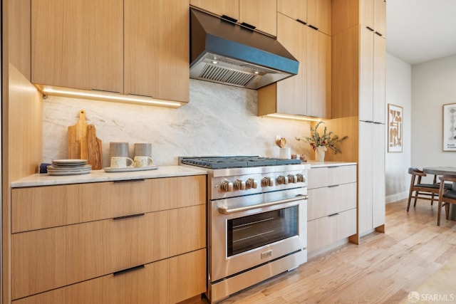 kitchen with tasteful backsplash, light wood-style flooring, custom range hood, high end range, and light countertops