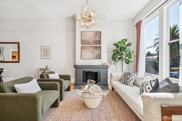 living room featuring a brick fireplace, a notable chandelier, and baseboards