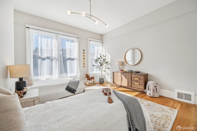 bedroom with an inviting chandelier, wood finished floors, visible vents, and baseboards