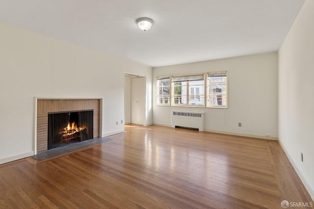 unfurnished living room with radiator heating unit, light hardwood / wood-style floors, and a brick fireplace