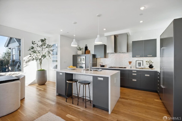 kitchen with decorative light fixtures, wall chimney range hood, gray cabinets, a kitchen island with sink, and high end refrigerator