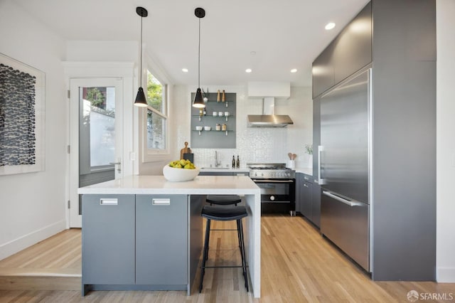 kitchen with wall chimney exhaust hood, tasteful backsplash, hanging light fixtures, a breakfast bar, and high quality appliances