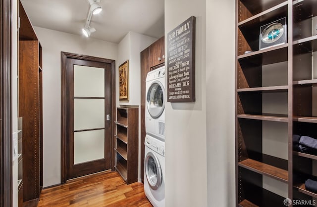 laundry area with track lighting, wood finished floors, stacked washer / dryer, and cabinet space