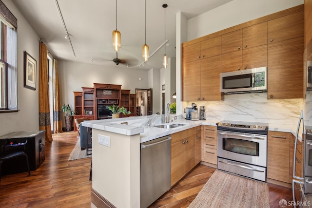 kitchen with a sink, dark wood-type flooring, a peninsula, tasteful backsplash, and appliances with stainless steel finishes