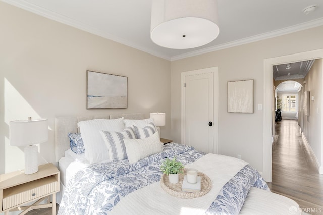 bedroom with crown molding, wood finished floors, arched walkways, and baseboards