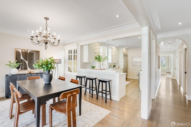 dining area featuring baseboards, light wood-style floors, arched walkways, and ornamental molding