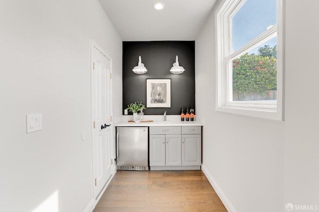 bar featuring baseboards, light wood finished floors, freestanding refrigerator, a sink, and indoor wet bar