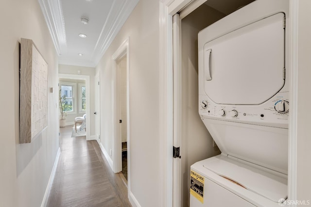 washroom with wood finished floors, baseboards, laundry area, stacked washer and clothes dryer, and crown molding