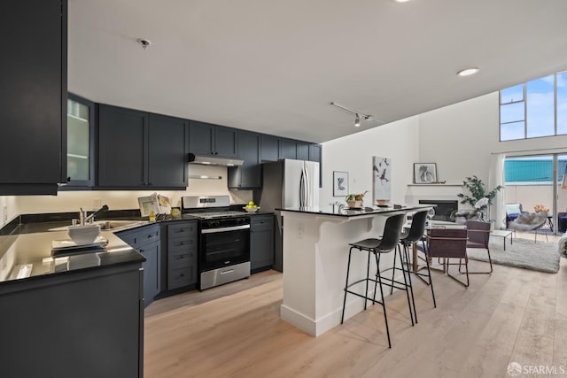 39 Boardman Pl Unit 105, San Francisco, CA 94103 - kitchen with stainless steel appliances, a breakfast bar area, dark countertops, under cabinet range hood, and light wood-type flooring