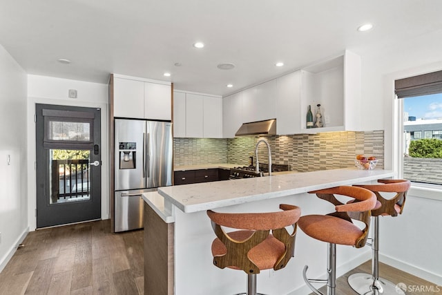 kitchen featuring a breakfast bar, white cabinetry, stainless steel fridge with ice dispenser, and kitchen peninsula