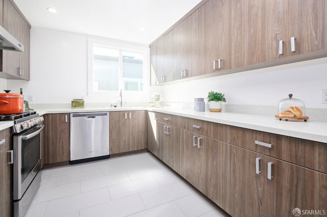 kitchen featuring light countertops, wall chimney exhaust hood, appliances with stainless steel finishes, and a sink