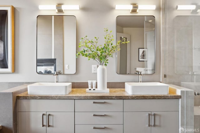 full bathroom featuring double vanity, a shower with shower door, and a sink