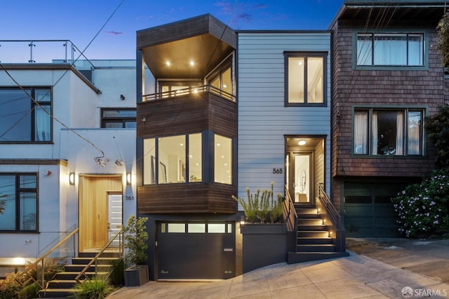 modern home featuring a garage, a balcony, driveway, and entry steps