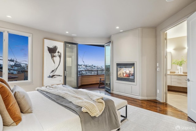 bedroom with recessed lighting, wood finished floors, a multi sided fireplace, and connected bathroom