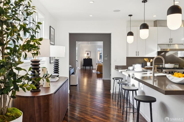 kitchen with dark countertops, decorative light fixtures, a breakfast bar, white cabinets, and dark wood-style flooring