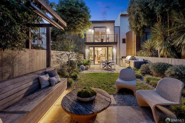 back of house with fence, outdoor lounge area, a balcony, a patio area, and an outdoor kitchen