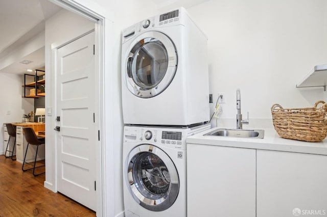 clothes washing area featuring wood finished floors, stacked washing maching and dryer, and a sink