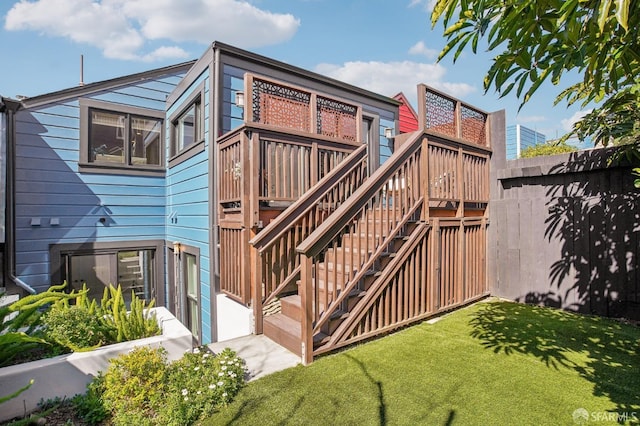 rear view of property featuring stairway, a wooden deck, a yard, and fence