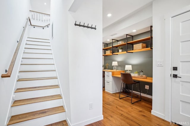 stairway with recessed lighting, wood finished floors, built in desk, and baseboards