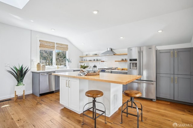 kitchen with butcher block countertops, stainless steel appliances, light wood-style floors, and wall chimney range hood