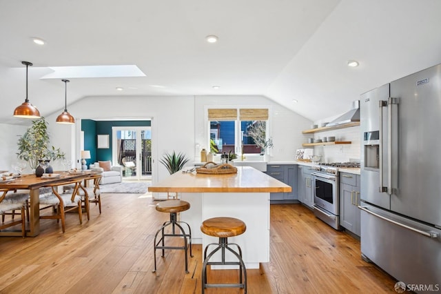 kitchen featuring stainless steel appliances, a kitchen bar, vaulted ceiling with skylight, and gray cabinets