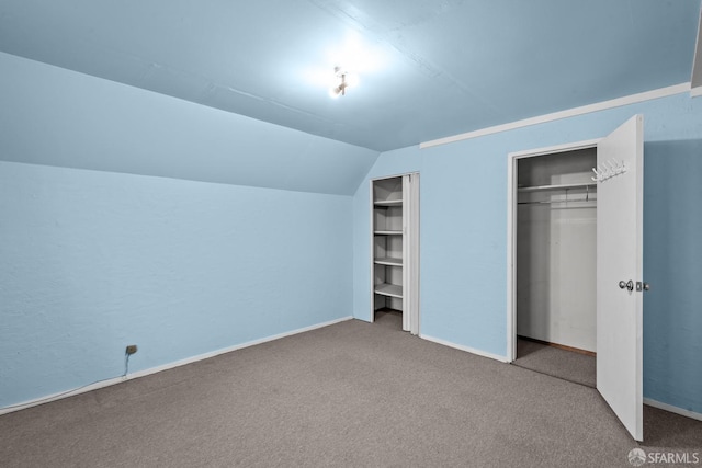 unfurnished bedroom with multiple closets, vaulted ceiling, and carpet floors