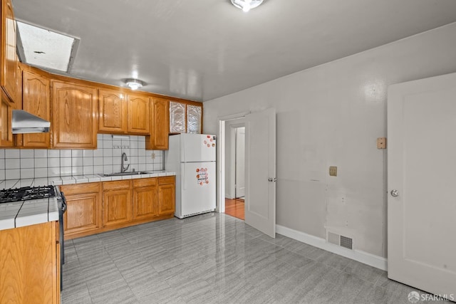 kitchen with sink, tile countertops, white refrigerator, range with gas stovetop, and backsplash