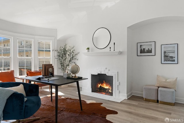 home office featuring baseboards, a fireplace with flush hearth, and wood finished floors