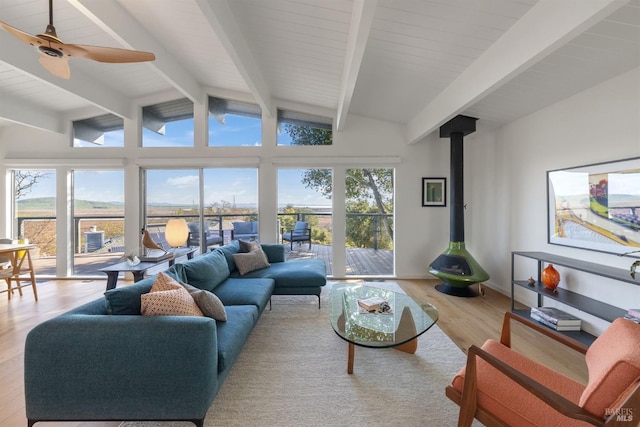 living area featuring vaulted ceiling with beams, ceiling fan, wood finished floors, baseboards, and a wood stove