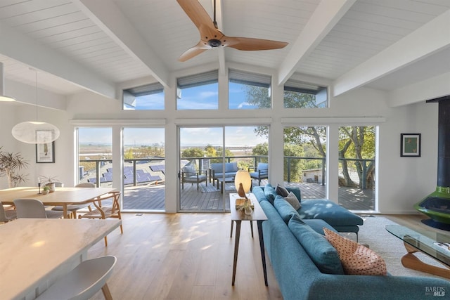 sunroom featuring vaulted ceiling with beams, ceiling fan, and a wood stove