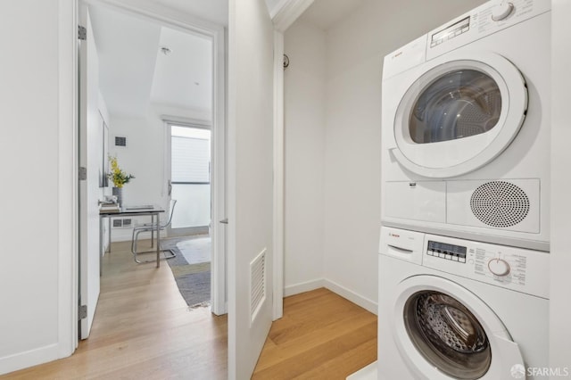 washroom with visible vents, stacked washer and dryer, light wood-style flooring, and baseboards